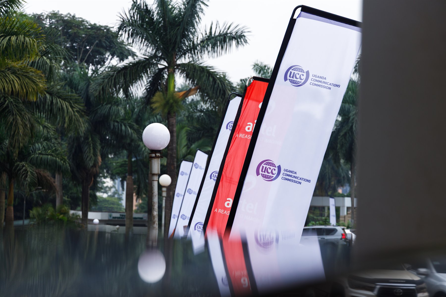 Architectural reflection view of the Uganda Communications Commission (UCC) and partner feather flag array lining the venue arrival.